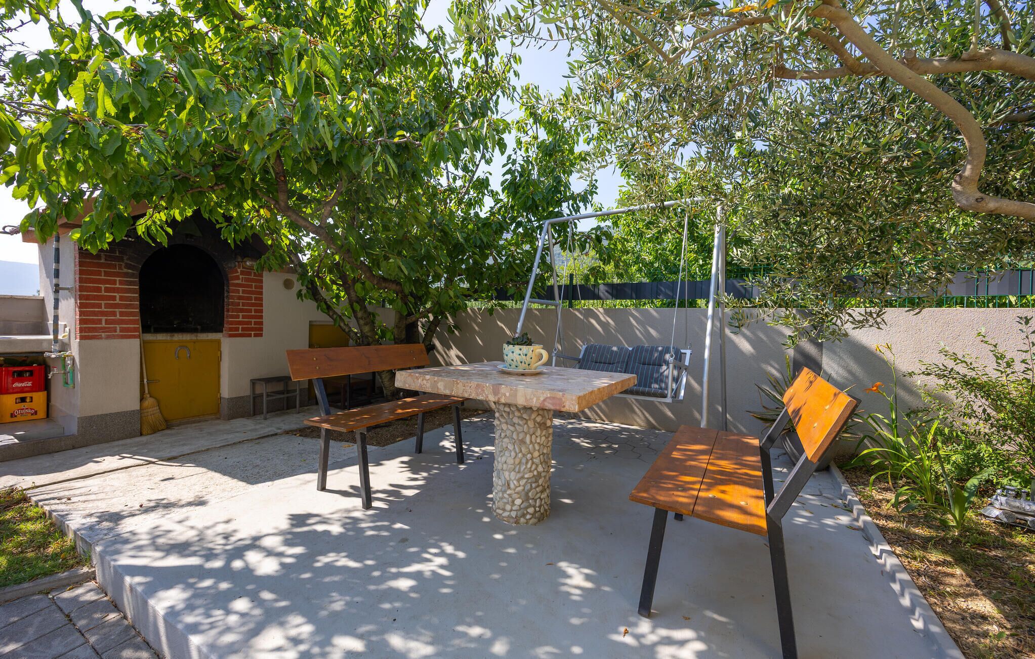 Una terrazza esterna con tavolo in pietra, panche di legno e un'amaca.