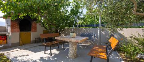 Una terrazza esterna con tavolo in pietra, panche di legno e un'amaca.