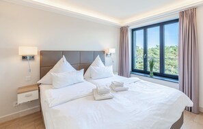 A hotel room with a large bed, two bedside tables, a nightstand, a window with curtains, and a view of trees. - Awesome apartment in Binz with indoor swimming pool (Prora/Rügen)