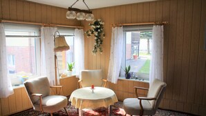A room with wooden paneled walls, a round table with a white tablecloth, two chairs, a hanging lamp, and a potted plant.