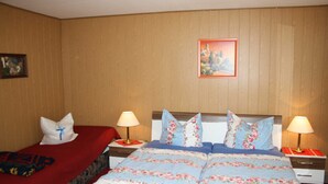 A hotel room with two beds, each with a different colored bedspread. There are two bedside tables with lamps, a framed picture on the wall, and a wooden panel wall.