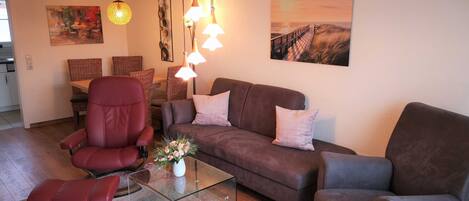 A living room with a sofa, armchair, glass coffee table, and a painting on the wall.