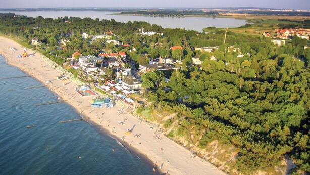Vue aérienne d’une zone côtière comprenant une plage, des immeubles résidentiels et une zone boisée.