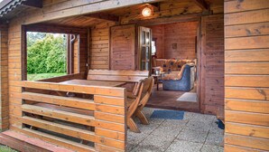 Une cabane en bois avec un banc et un canapé à l’intérieur, une porte donnant sur une autre pièce et une fenêtre donnant sur la verdure.
