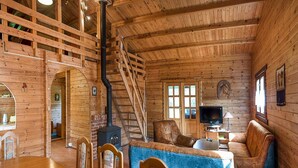 L’intérieur d’une cabane en rondins, avec une cheminée, un escalier en bois et un coin salon confortable.