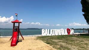 Una playa con una torre de salvavidas, un cartel grande que dice "BALATONERODAR" y una vista despejada del mar.