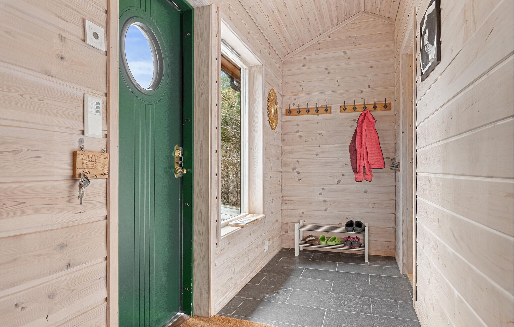 Un intérieur en bois avec une porte verte, une fenêtre, un porte-manteau et un meuble à chaussures.