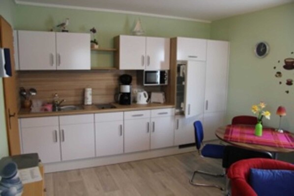 A compact kitchen with white cabinets, a microwave, and a coffee maker. There is a dining area with a table and chairs, and a small window with a view of the outside.