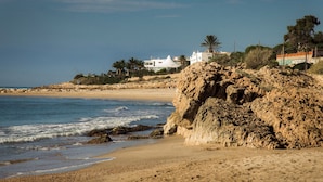 Una playa con acantilados rocosos, una orilla arenosa y edificios al fondo.