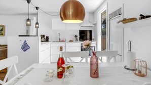 A modern kitchen with white cabinetry, a large copper pendant light, and a dining area with a white table set for two. - Nice home in Aakirkeby with WiFi (Aakirkeby)