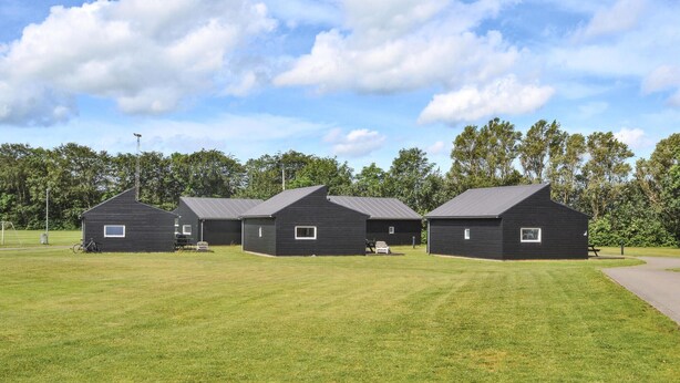 Een rij van drie zwarte houten vakantiehuisjes met puntige daken, gelegen in een grasveld met bomen op de achtergrond.