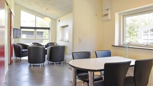 Een vergaderruimte met een ronde tafel en zwarte stoelen, grote ramen met zonwering en een plafond met inbouwverlichting.