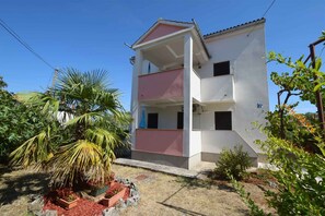 Un immeuble à plusieurs étages doté d’un balcon au deuxième étage, entouré de verdure et surplombant un ciel dégagé.