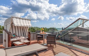 Une terrasse sur le toit dotée d’une balustrade en verre, de chaises longues, d’un auvent à rayures et d’une table avec des boissons.