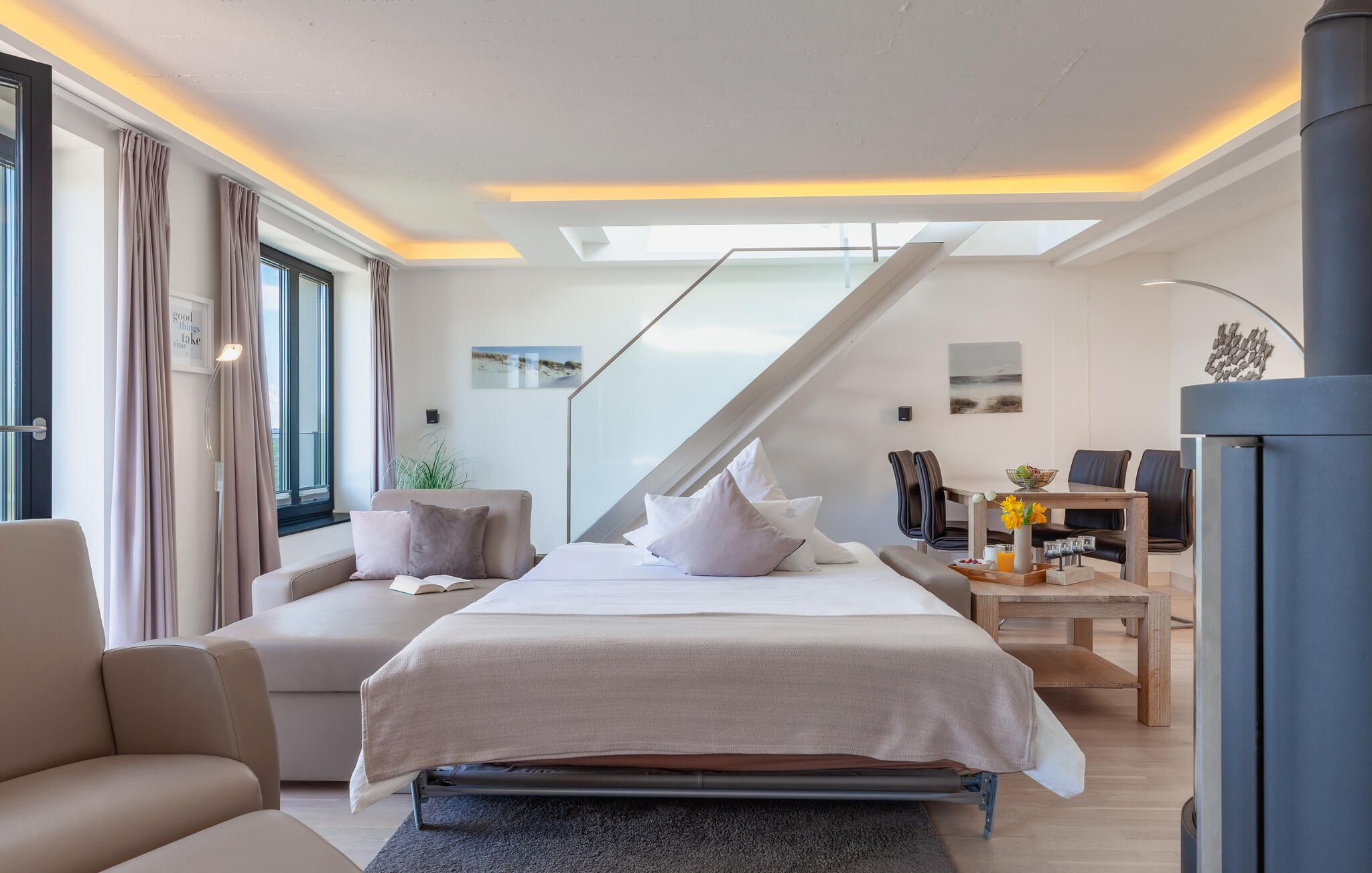A modern bedroom with a bed, two sofas, a desk, and a staircase.