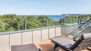 A balcony with a glass railing, lounge chairs, and a view of the sea and trees. - Pet friendly apartment in Binz with house sea view (Prora/Rügen)