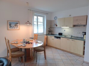 Una cocina moderna con comedor, que incluye una mesa redonda, sillas, una ventana y armarios de tonos claros.