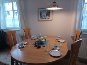 A dining area with a round table, chairs, a painting, and a window with curtains.