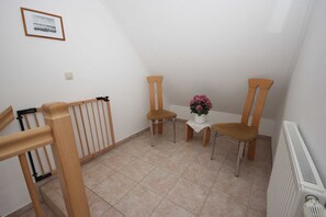 Une petite pièce propre, avec une chaise en bois, une petite table sur laquelle est posé un vase de fleurs et un radiateur.