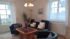 A living room with a sofa, two armchairs, a coffee table, a floor lamp, a potted plant, and a window with curtains. - By the Sea, Port Side - By the Sea - Port Side (Wustrow)