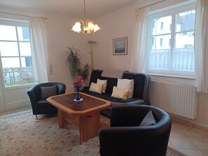 A living room with a sofa, two armchairs, a coffee table, a floor lamp, a potted plant, and a window with curtains. - By the Sea, Port Side - By the Sea - Port Side (Wustrow)