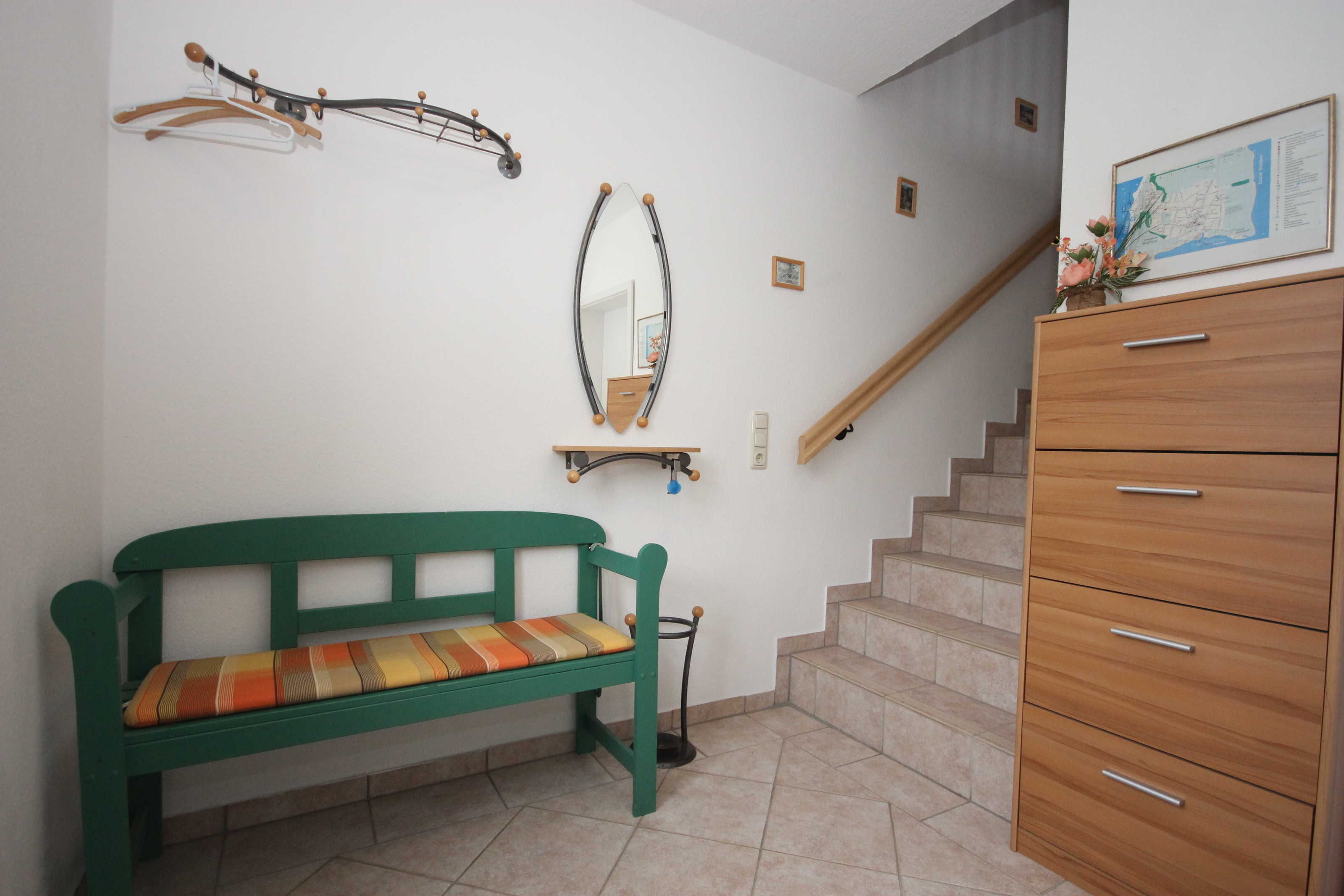 A room with a green bench, a wooden dresser, a mirror, and a staircase.