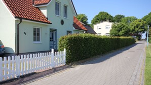 A street with houses, a white picket fence, and a paved road. - By the Sea, Port Side - By the Sea - Port Side (Wustrow)
