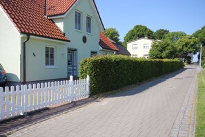 A street with houses, a white picket fence, and a paved road. - By the Sea, Port Side - By the Sea - Port Side (Wustrow)