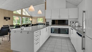 A modern kitchen with white cabinets, a large island, and a dining area with black chairs. - Nice home in Sydals with sauna (Sydals)