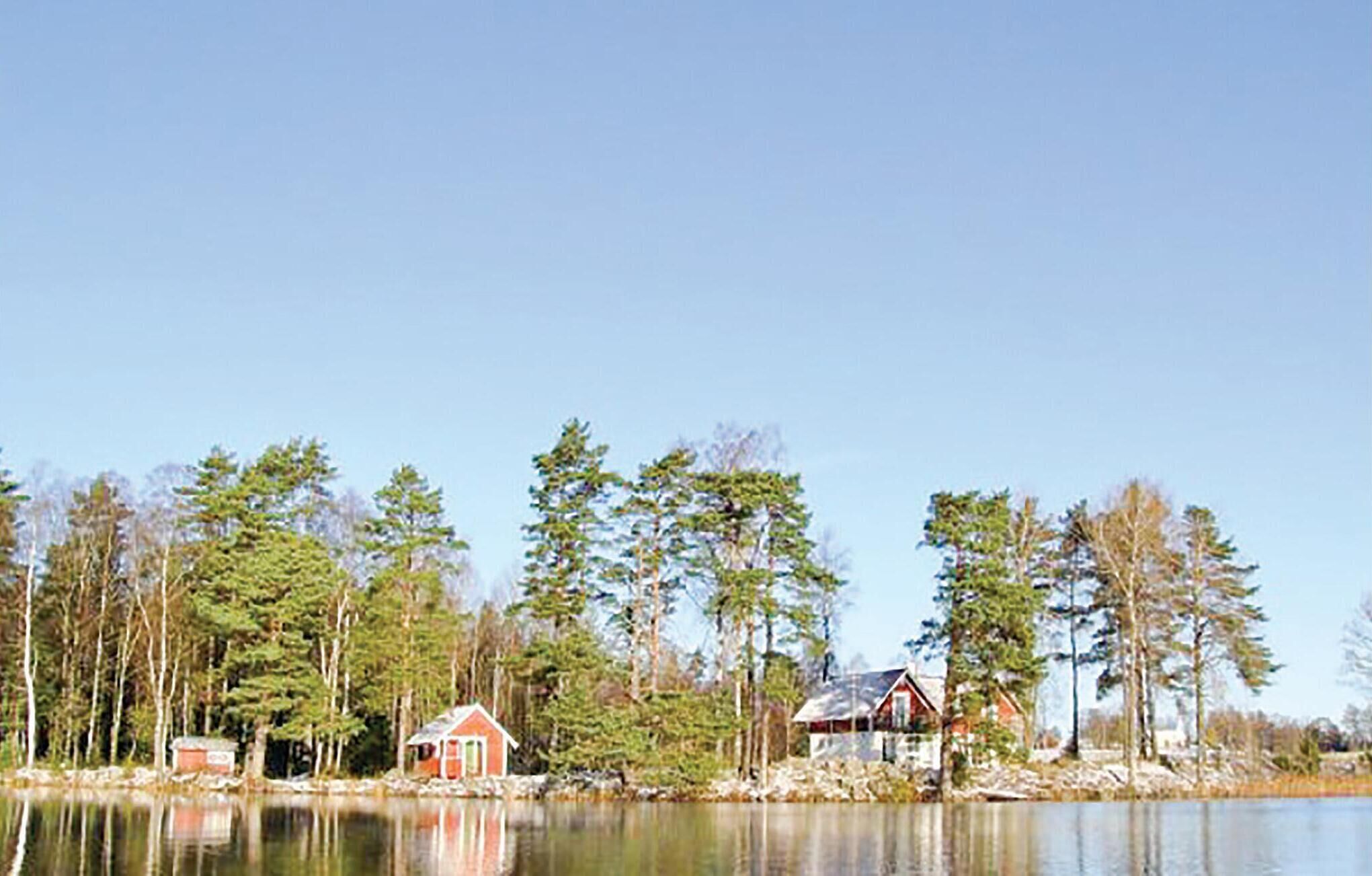 Una cabaña junto al lago con un pequeño muelle, rodeada de un bosque frondoso y cielos despejados.