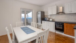 Una cucina compatta con mobili bianchi, un frigorifero in acciaio inossidabile, un forno a microonde, un tostapane e un forno. C'è un tavolo con sedie e una vista all'esterno tramite una porta vetrata.