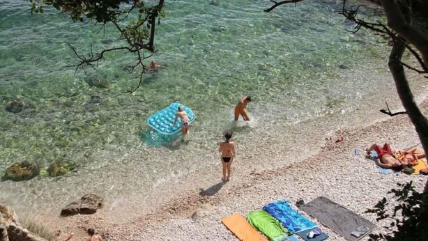 A beach with clear water, people swimming, and a floating pool.