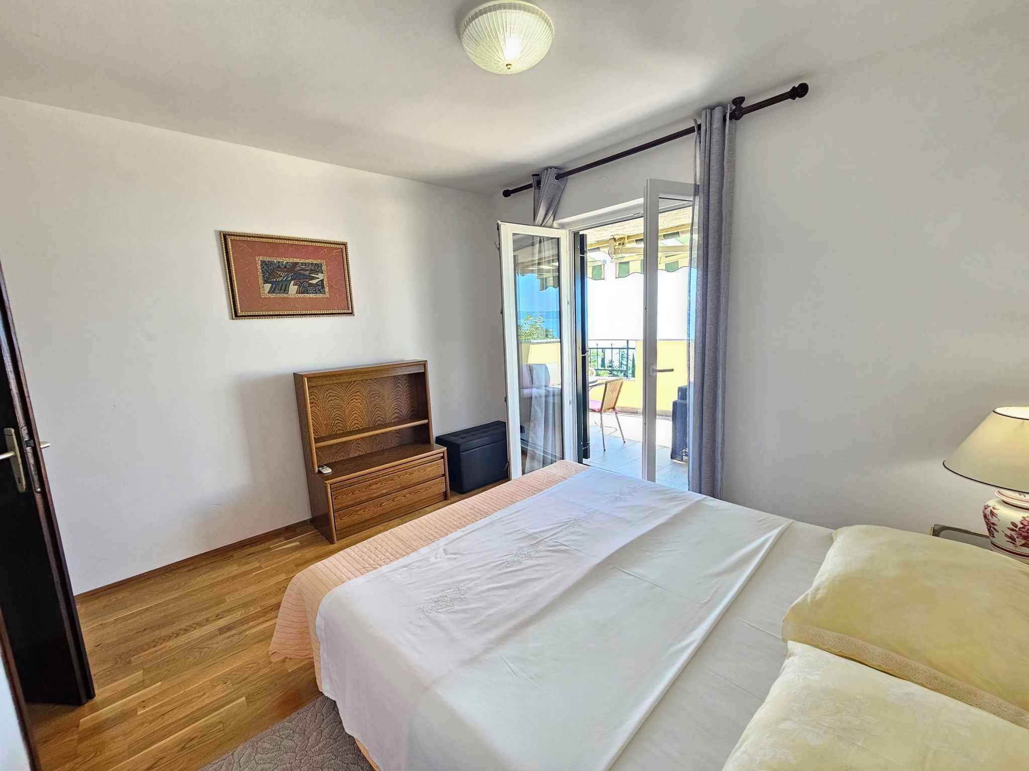 Un dormitorio con cama, cómoda de madera, una mesita y un balcón con vistas.