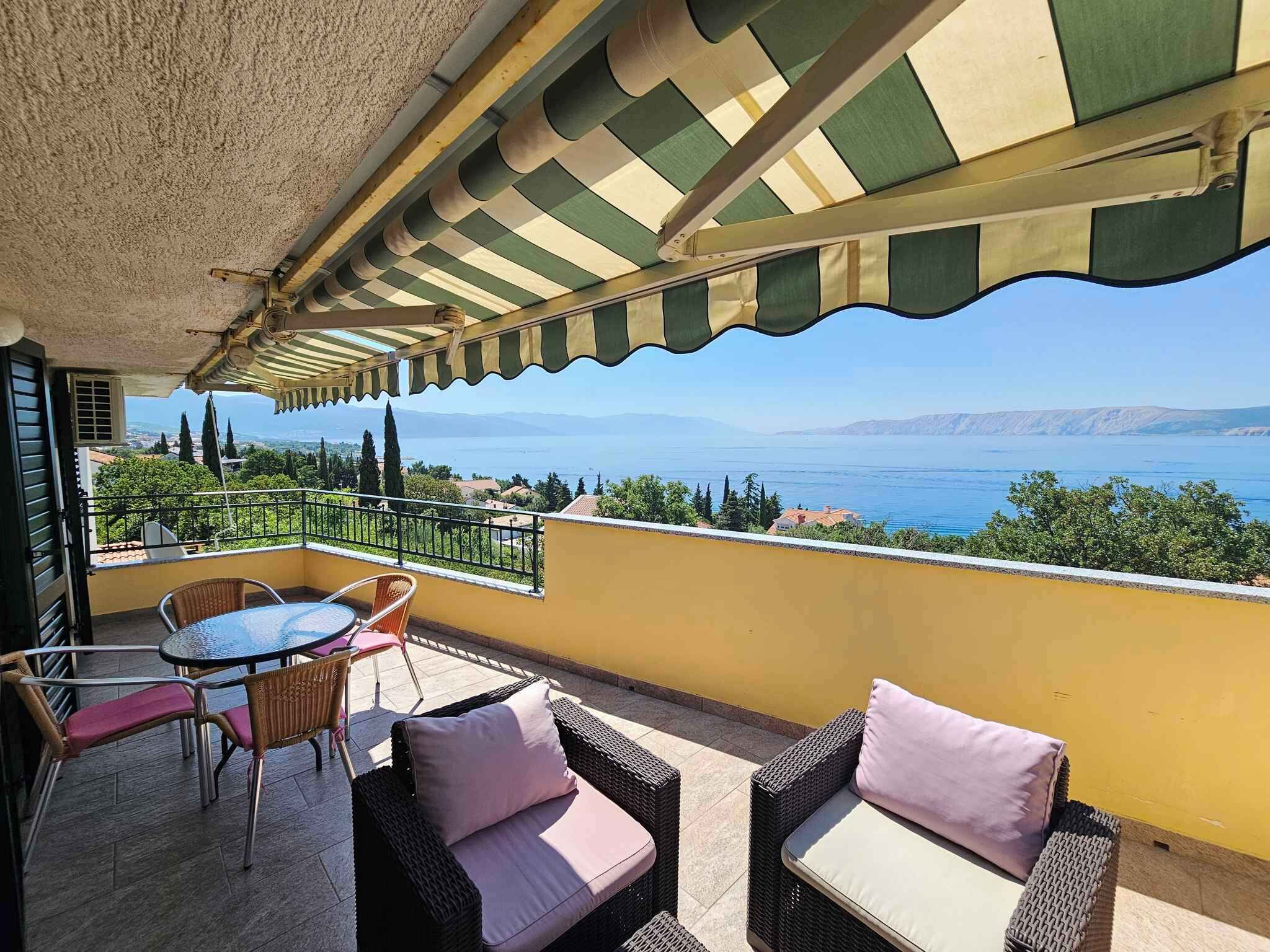 A balcony with wicker furniture, a view of the sea, and a clear sky.