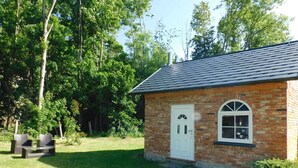 A small brick building with a white door and a window, surrounded by a grassy yard and trees. - Holiday apartment with a view of the Franconian Forest (Blankenstein)