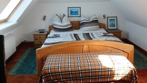 A bedroom with a sloped ceiling, a bed with a plaid bedspread, a bedside table with a lamp, and a framed picture on the wall. - Holiday apartment with a view of the Franconian Forest (Blankenstein)
