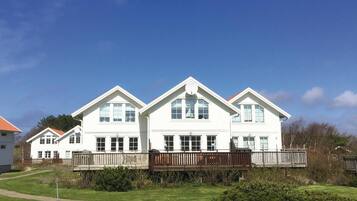 Une grande maison blanche à deux étages, dotée d’une façade symétrique, de nombreuses fenêtres et d’une terrasse en bois.