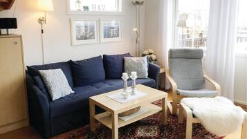 Un salon avec un canapé bleu foncé, une table basse en bois clair, un fauteuil gris et un tapis à motifs.