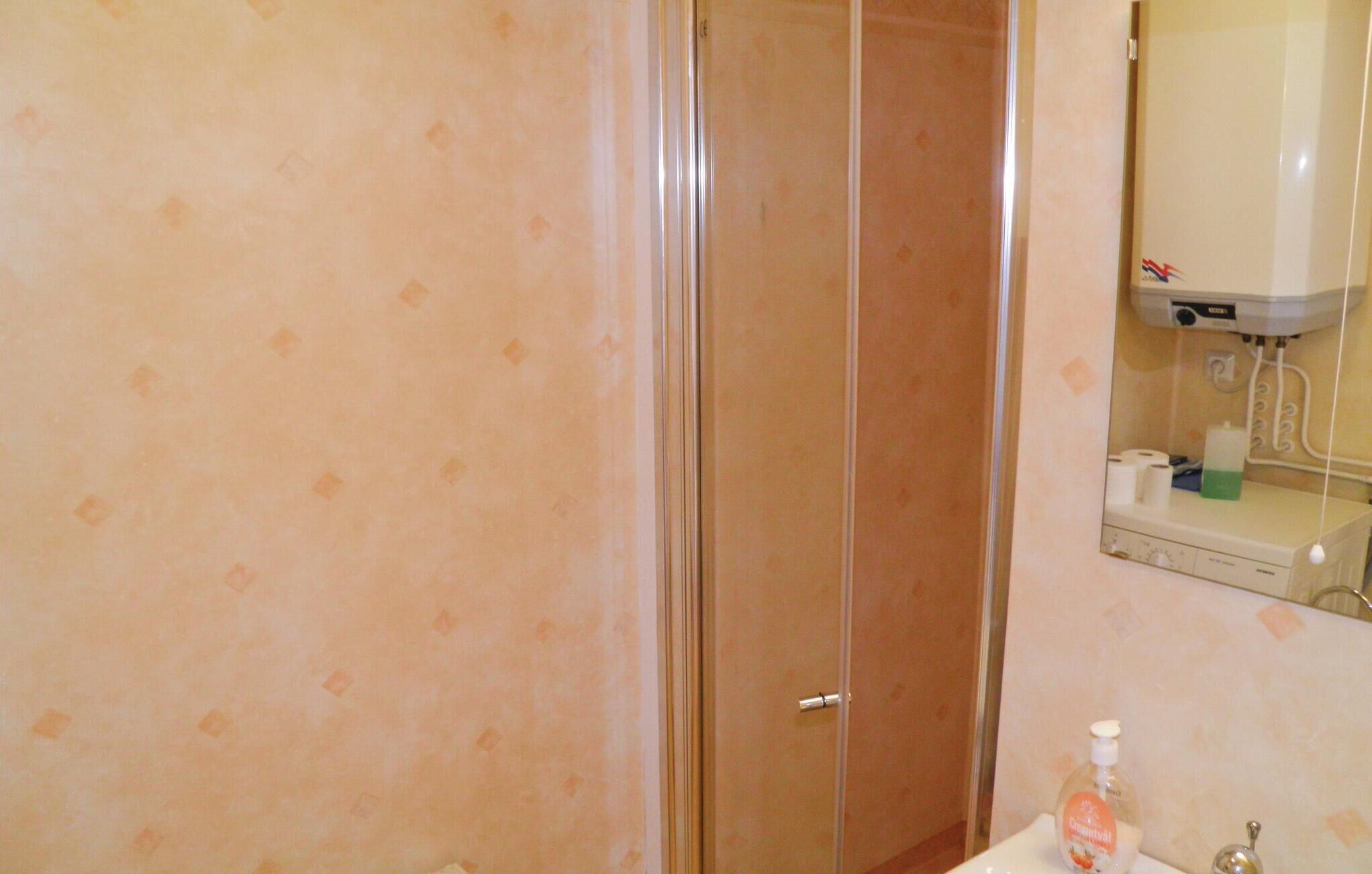 Ein Badezimmer mit Duschabtrennung aus Glas, einem Waschbecken mit Seifenspender und einem Spiegel, an dem ein Handtuch hängt.