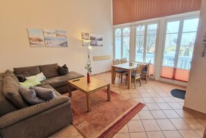 Sala de estar con sofá, mesa de centro y mesa de comedor. Amplias ventanas con vistas al exterior.