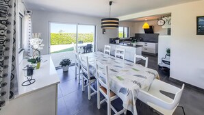 Een moderne eethoek met een lange tafel, witte stoelen en uitzicht op groen.