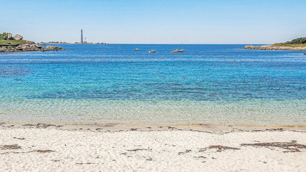 Een strand met helderblauw water, boten en rotsachtige landtongen.