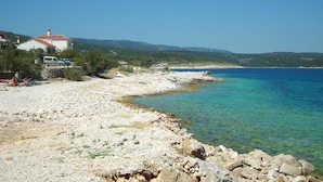 A coastal area with a rocky beach, clear blue water, and a building with a red roof. - Gorgeous home in Povlja (Povlja)