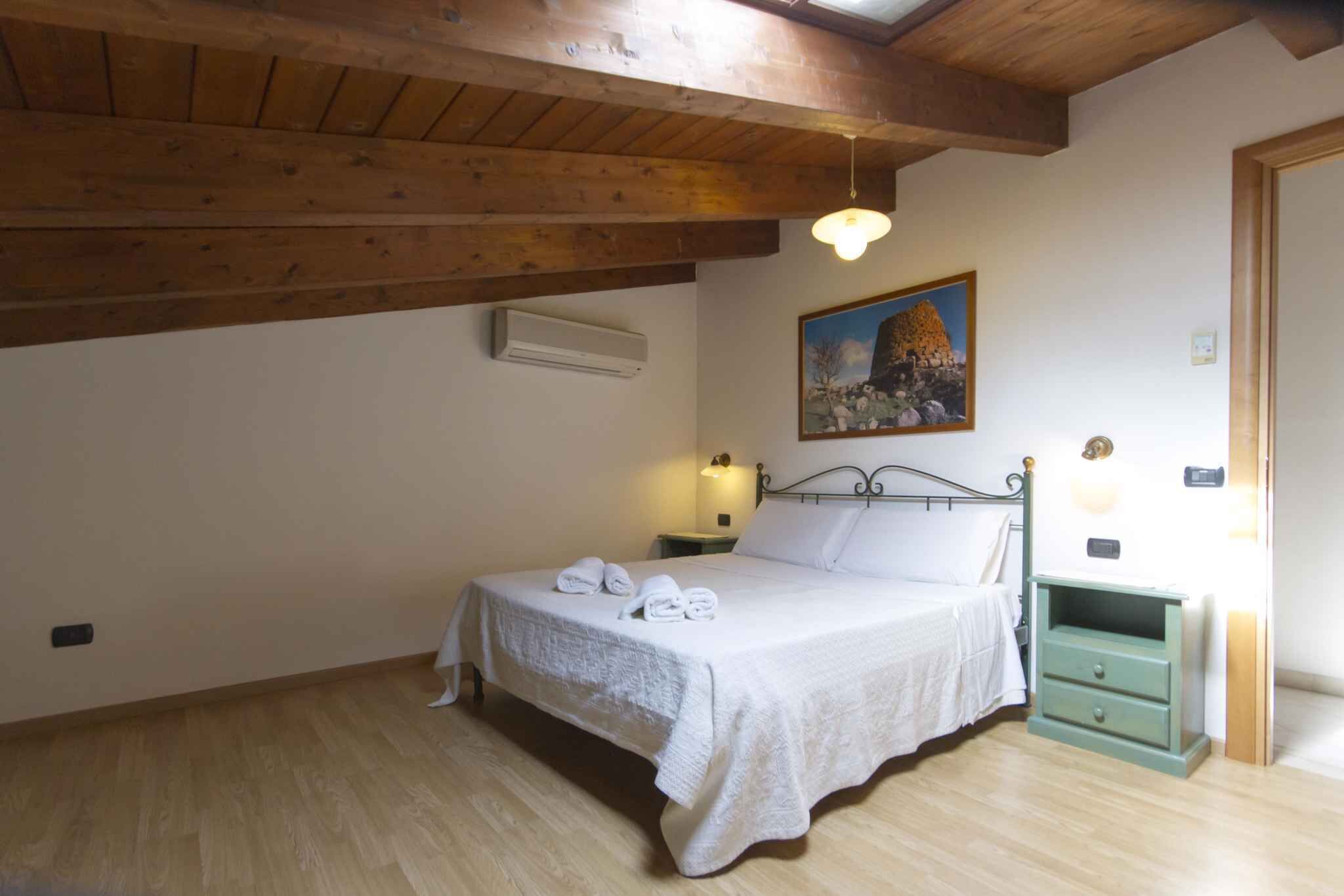 Una camera da letto con soffitto in legno, un letto con lenzuola bianche, un comodino con lampada e un quadro appeso al muro.