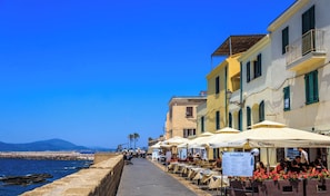 A seaside promenade with outdoor seating, a stone wall, and buildings with balconies.