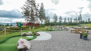 A golf course with a wooden bench, a picnic table, and a red building in the background. - Stunning home in Trysil with sauna (Trysil)