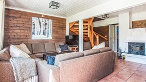 A cozy living room with a wooden wall, a large sofa, a coffee table, and a fireplace. - Stunning home in Trysil with sauna (Trysil)