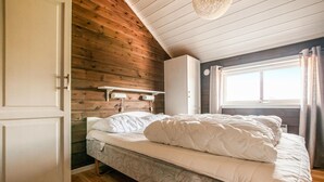 A bedroom with a wooden ceiling, a bed with white bedding, a nightstand, and a window with curtains. - Stunning home in Trysil with sauna (Trysil)