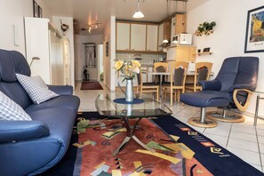 Un salon moderne avec un canapé bleu, une table basse en verre et un tapis aux couleurs vives.