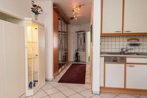 Une cuisine avec des meubles blancs, un pare-feu en carrelage, un lave-vaisselle encastré et un tapis rouge.